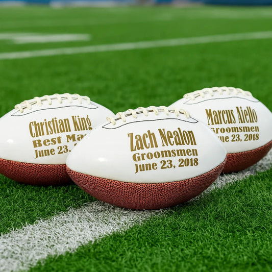Three footballs with personalized names and dates on a grass field