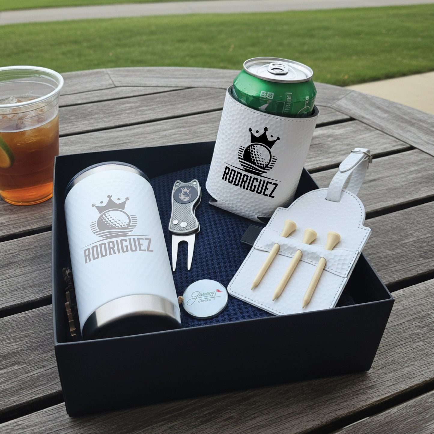 Golf-themed gift set with engraved tumbler, can cooler, divot tool, cigar case, and ball marker displaying sample name Rodriguez and crown golf logo design.