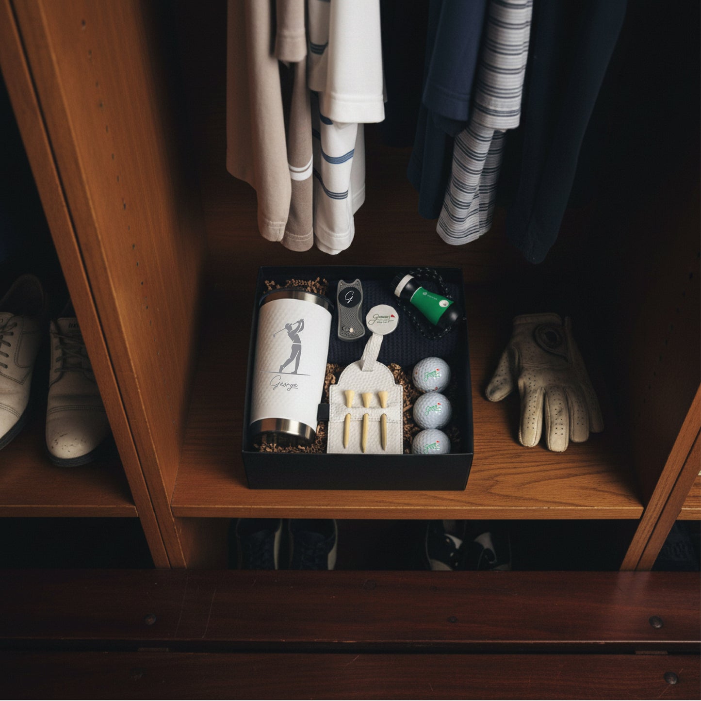Golf-themed gift box with engraved flask, divot tool, golf balls, and accessories displayed on wooden shelf with clothing and shoes.