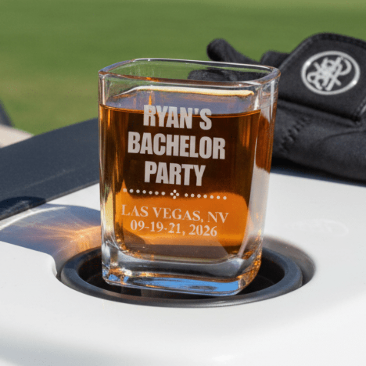 Personalized glass with 'Ryan's Bachelor Party' text on a car cup holder with a blurred background