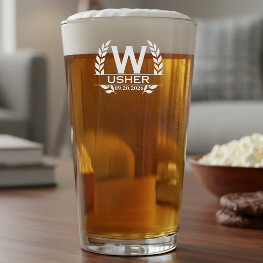 Pint glass with 'Usher' text and date, filled with beer, on a table with popcorn and cookies.