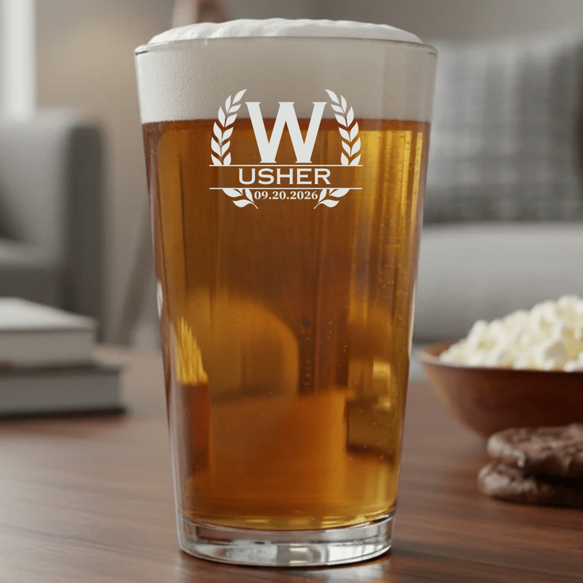 Pint glass with 'Usher' text and date, filled with beer, on a table with popcorn and cookies.