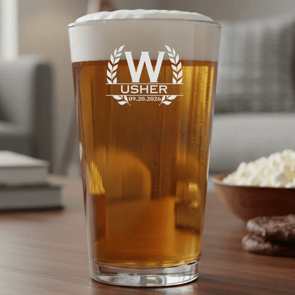 Pint glass with 'Usher' text and date, filled with beer, on a table with popcorn and cookies.