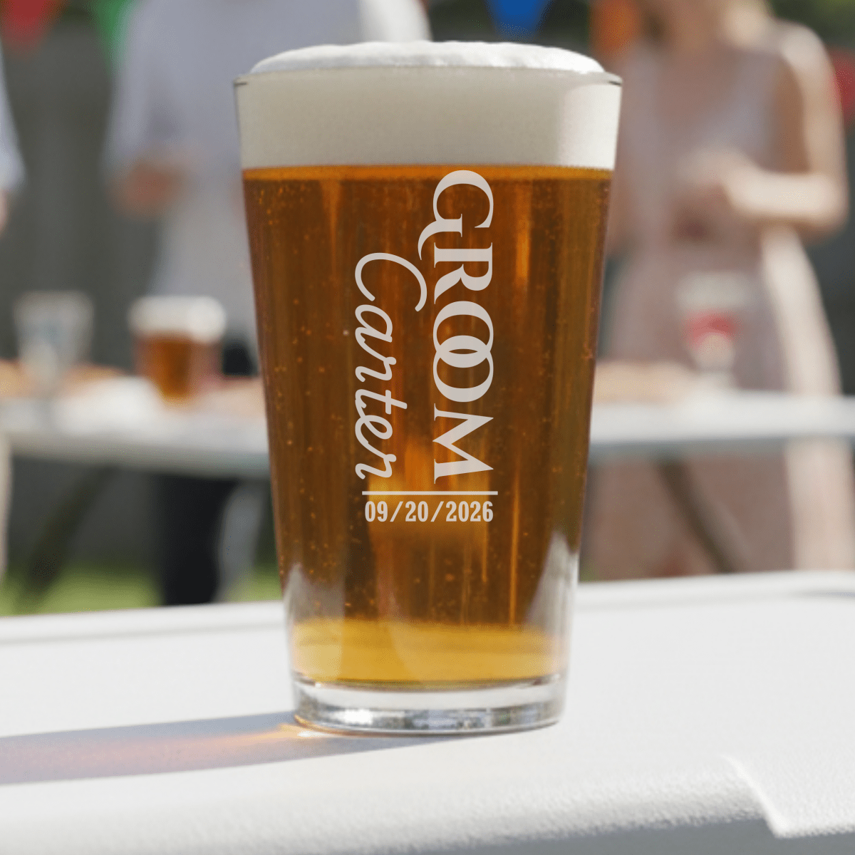 Pint glass with 'Groom Carter 09/20/2026' text on a blurred outdoor background