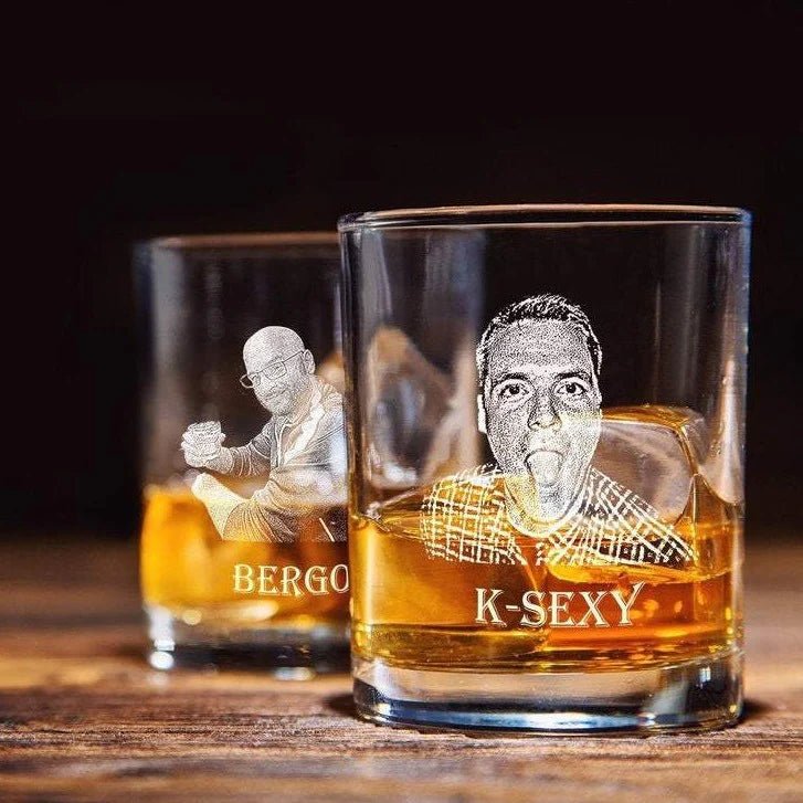 Two glasses with engraved faces and names filled with a amber liquid on a wooden surface.