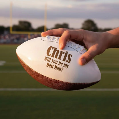 Hand holding a football with 'Chris Will you be my Best Man?' text on a sports field.
