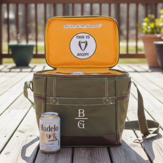 Green cooler bag with open lid showing 'Will You Be My Groomsman?' question, 'Chug to Accept' sticker, and a can of Modelo beer on a wooden deck.