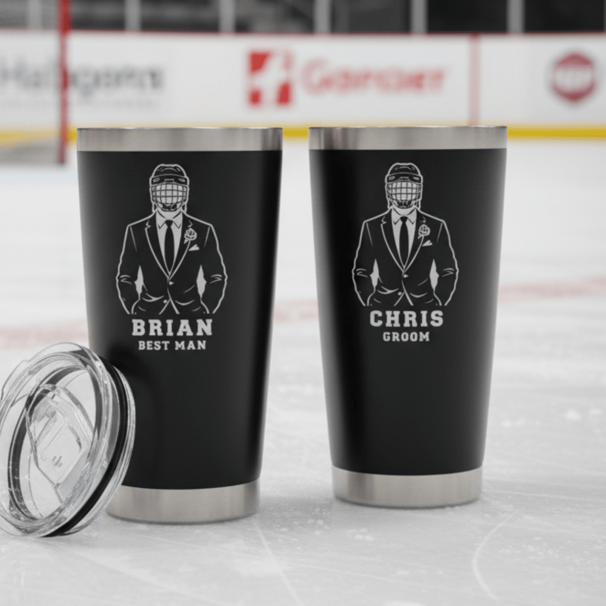 Two black tumblers with engraved designs and names on a hockey rink background