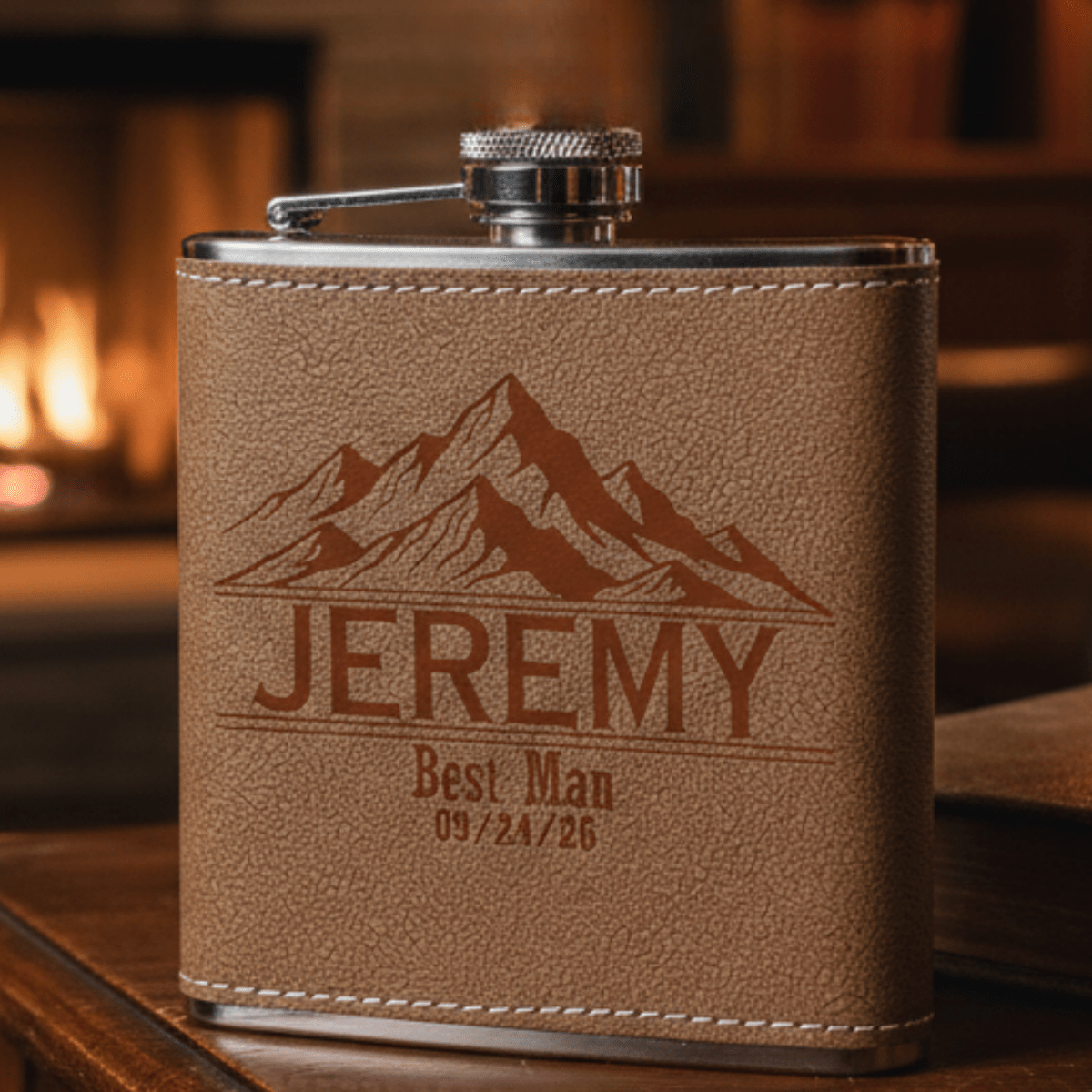 Brown leather flask with engraved mountain design and text on a wooden surface.
