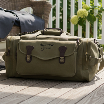 Tan canvas duffle bag with burgundy leather accents and brass hardware, personalized with sample engraving "Andrew" and "Groom" on front flap, displayed on wooden deck.