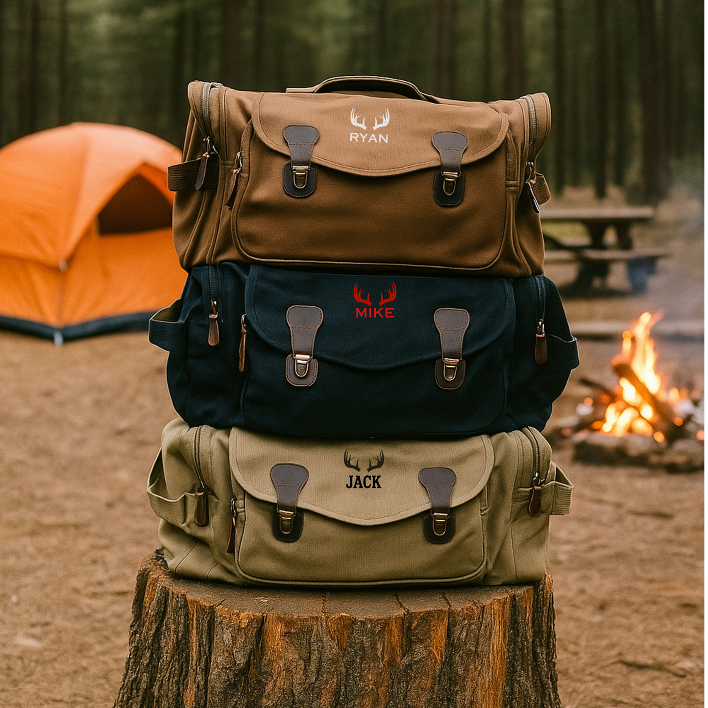 Three canvas duffle bags stacked on a wood log, each personalized with sample names "RYAN," "MIKE," and "JACK" embroidered with antler motifs in brown, navy, and khaki colors.