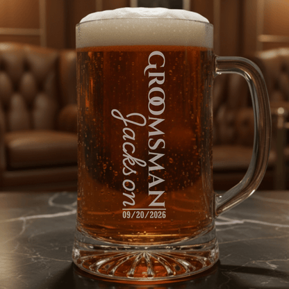 Personalized glass mug with beer and 'Groomsman Jackson' engraving on a marble surface.