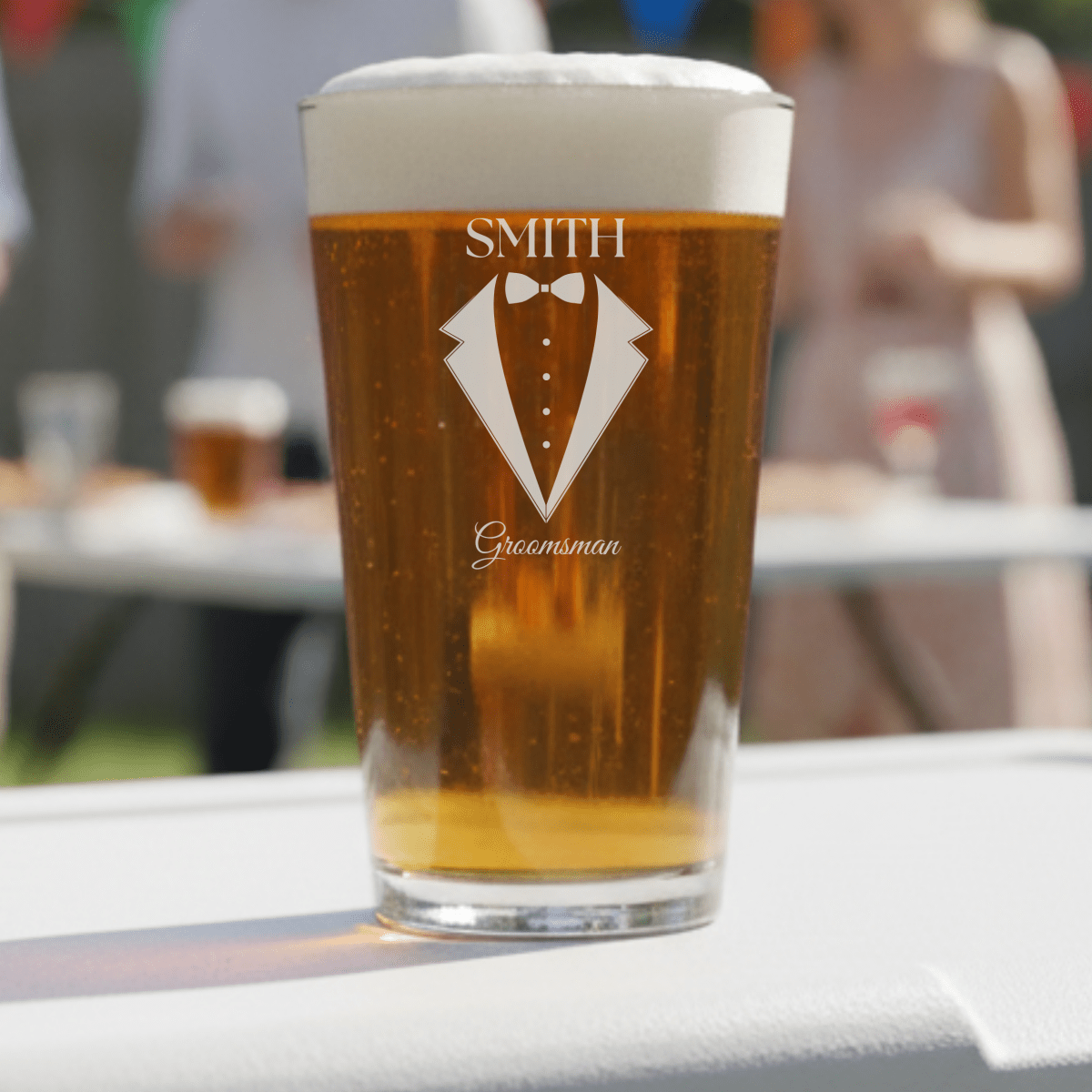 Pint glass with 'Smith Groomsman' design filled with beer on a table outdoors.