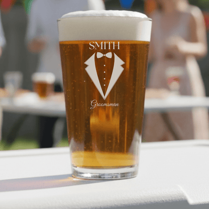 Pint glass with 'Smith Groomsman' design filled with beer on a table outdoors.