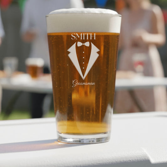 Pint glass with 'Smith Groomsman' design filled with beer on a table outdoors.