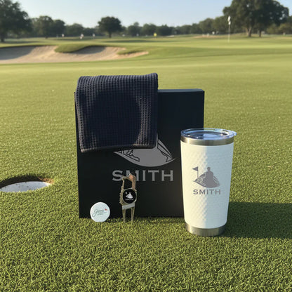Golf-themed gift set with personalized tumbler engraved "SMITH", navy towel, divot tool, and golf ball on course green.
