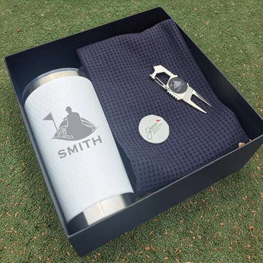 Golf-themed gift set with tumbler, towel, and divot tool in a box on grass.