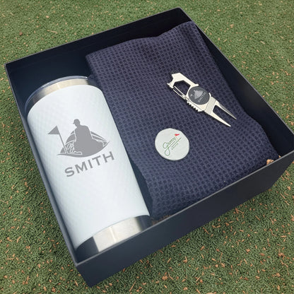 Golf-themed gift set with tumbler, towel, and divot tool in a box on grass.