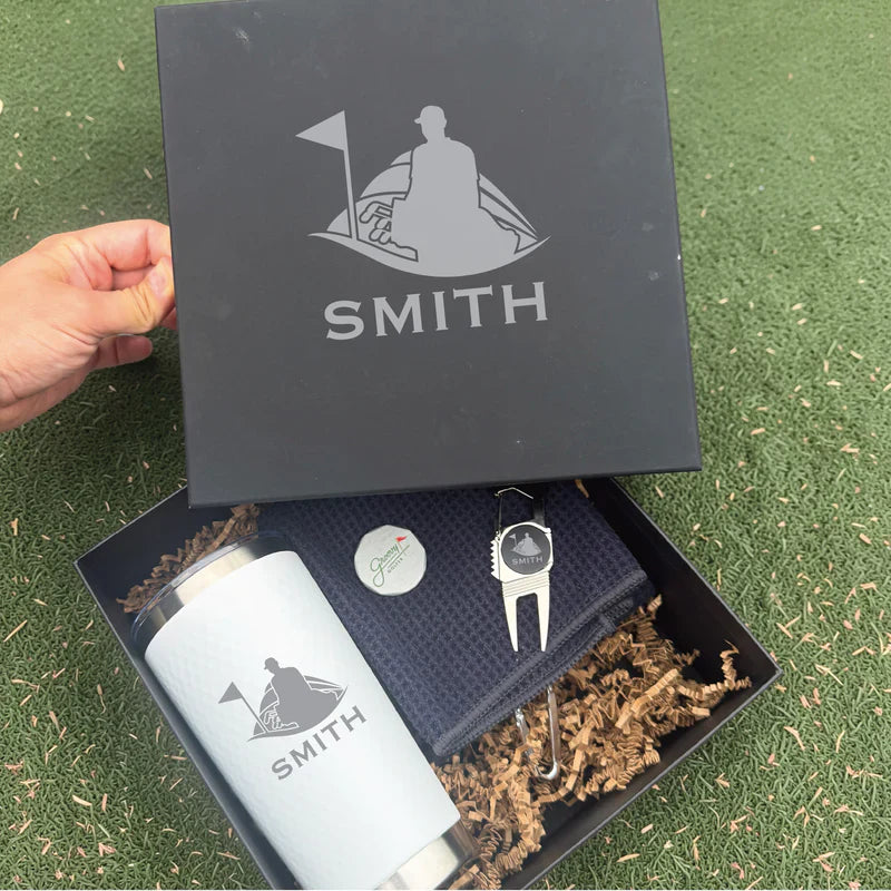 Personalized golf-themed gift box with engraved flask, divot tool, and ball marker showing sample name "SMITH" with golfer and flag design.