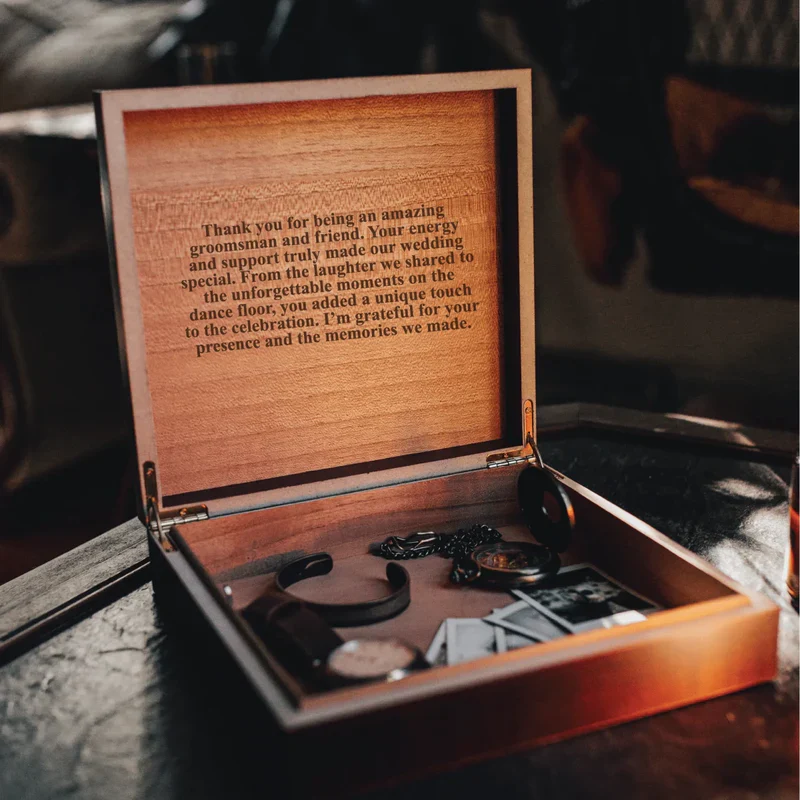 Open wooden keepsake box with engraved thank you message on interior lid and accessories inside, sample personalization for groomsman gift.