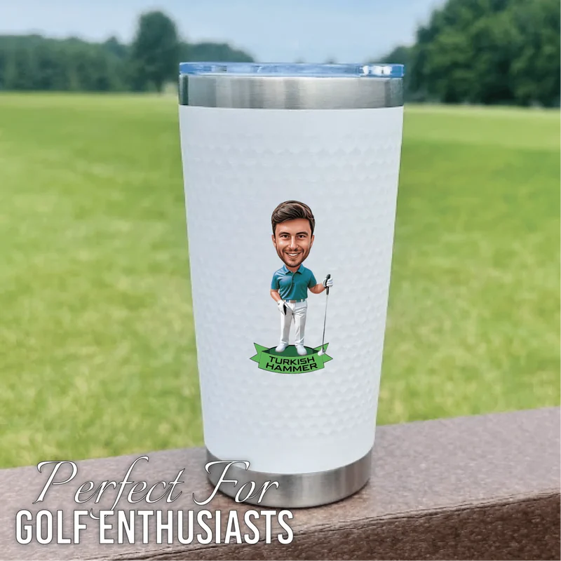 White insulated tumbler with stainless steel base featuring sample caricature of golfer with "Turkish Hammer" text on front, displayed outdoors with green field background.