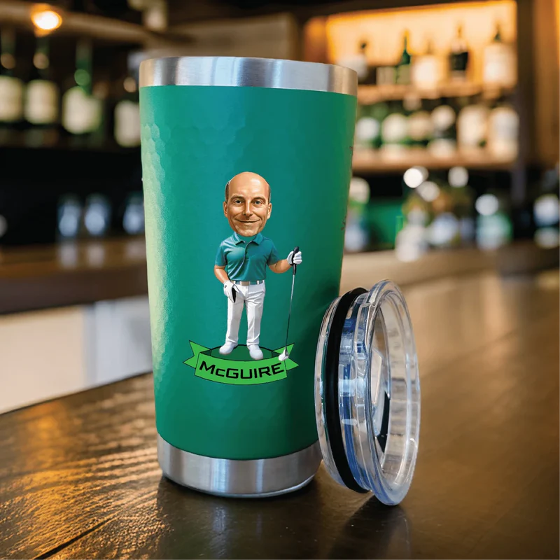 Green insulated tumbler with stainless steel band featuring custom caricature of golfer and sample name "McGuire" on banner, lid removed beside cup.