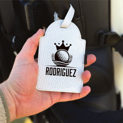 White leather golf gift box with crown and golf ball logo, personalized with sample name "RODRIGUEZ" in black engraving, held in hand with ribbon loop handle