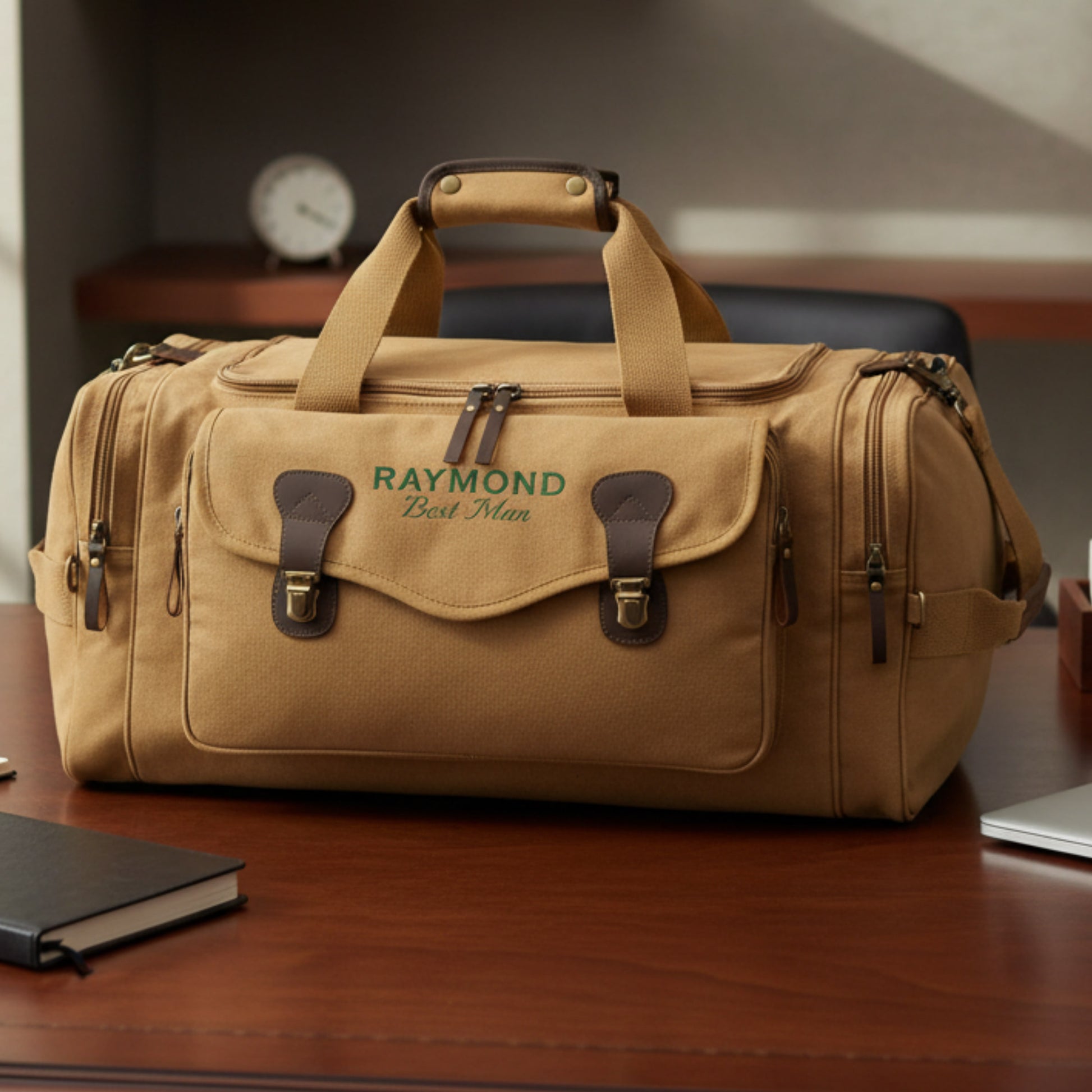 Tan canvas duffle bag with leather handles and brown leather accents, personalized with sample text "RAYMOND Best Man" on front panel, displayed on wooden desk.