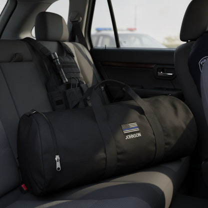 Black duffle bag with "JOHNSON" and Thin Blue Line flag embroidered on side, placed on vehicle back seat