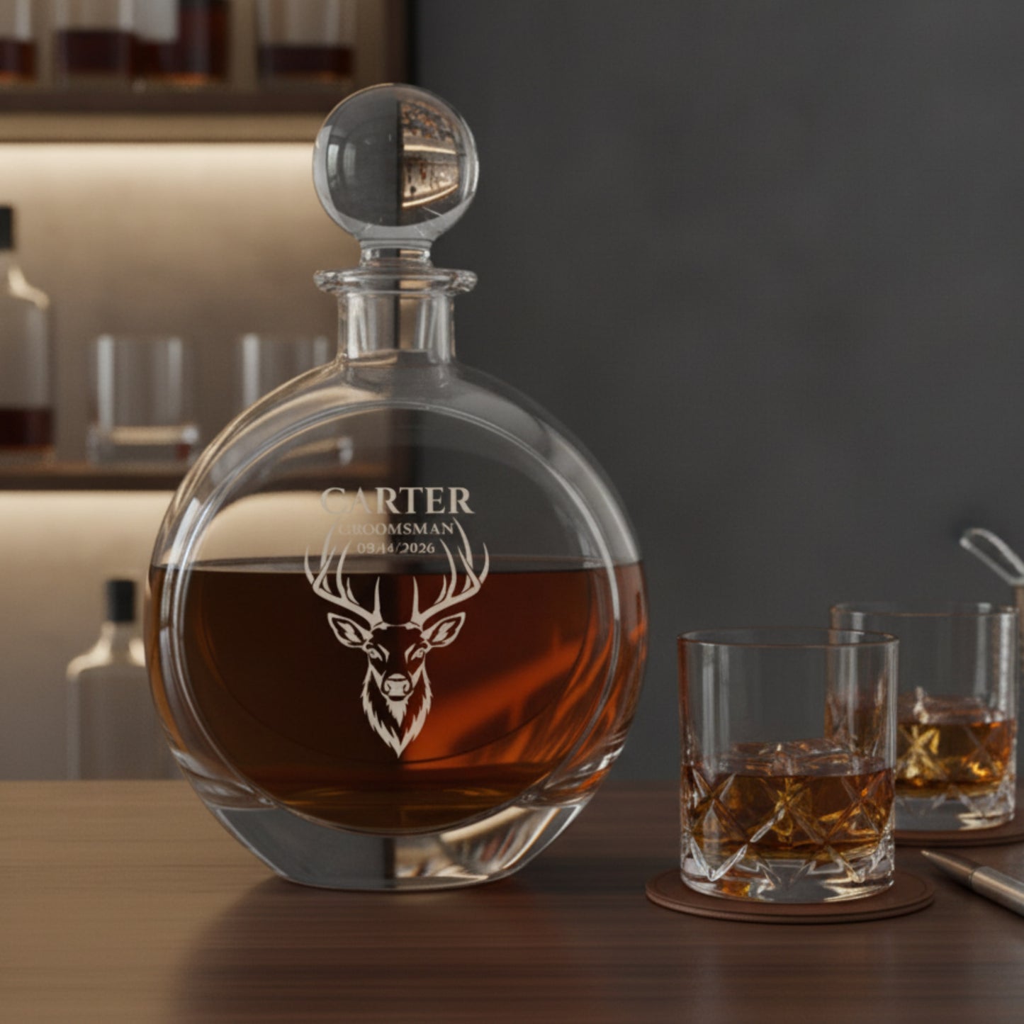Engraved decanter with stag head design and sample personalization reading "CARTER GROOMSMAN 09/14/2026," filled with amber liquor and displayed with two matching glasses.