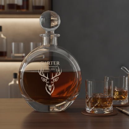 Engraved decanter with stag head design and sample personalization reading "CARTER GROOMSMAN 09/14/2026," filled with amber liquor and displayed with two matching glasses.