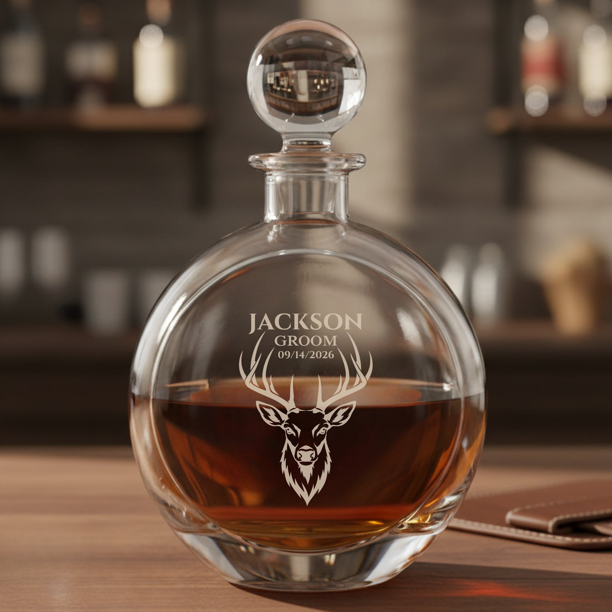 Engraved decanter with spherical stopper filled with amber liquor, featuring sample personalization reading "JACKSON GROOM 09/14/2026" above a stag head design
