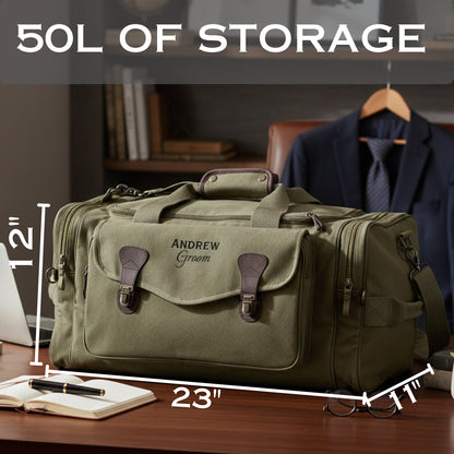 Olive canvas duffle bag with brown leather handles and accents, personalized with sample text "ANDREW Groom" on the front, displayed on wooden desk with dimensions marked showing 23" length and 12" height