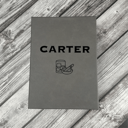 Gray leatherette box with "CARTER" engraved on cover and flask and cigar icons below, displayed on weathered wood surface