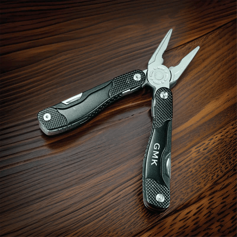 Multi-tool with black textured handles, stainless steel prongs, and sample engraving "CMK" on handle, displayed on dark wood surface.