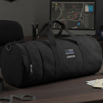 Black cylindrical duffle bag with sample personalization showing "JOHNSON" text and thin blue line flag emblem on front.