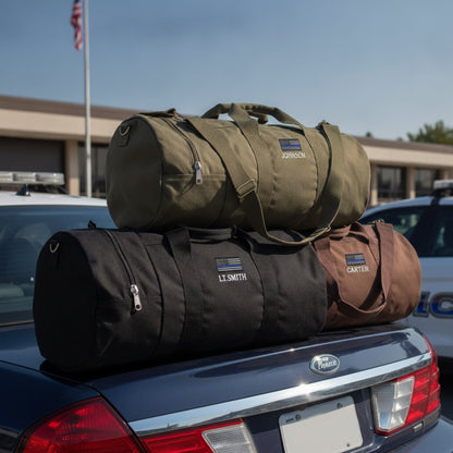 Three personalized canvas duffle bags stacked on a vehicle roof, with sample names "JOHNSCN," "LT.SMITH," and "CARTER" embroidered with American flag patches.