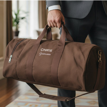 Brown canvas duffel bag with sample personalization reading "CHRIS" and "Groomsman" in white embroidery, held by man in gray suit.