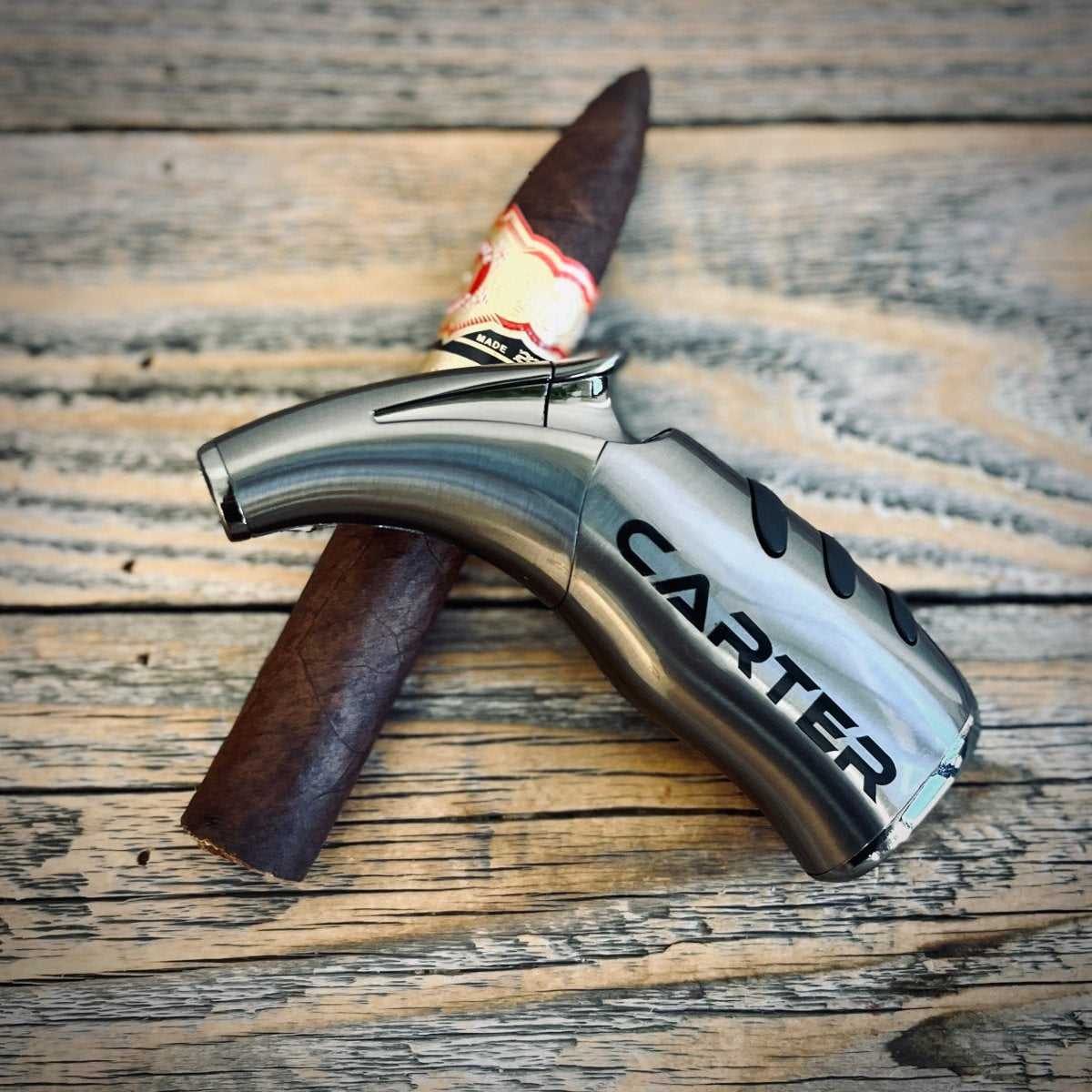 Stainless steel engraved flask with "CARTER" sample text displayed with a cigar on weathered wood surface.