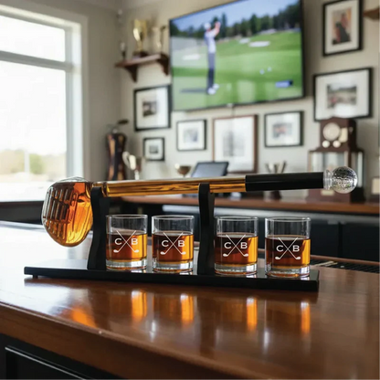 Personalized whiskey decanter set with golf club handle and four engraved glasses displaying sample monogram on wooden desk.