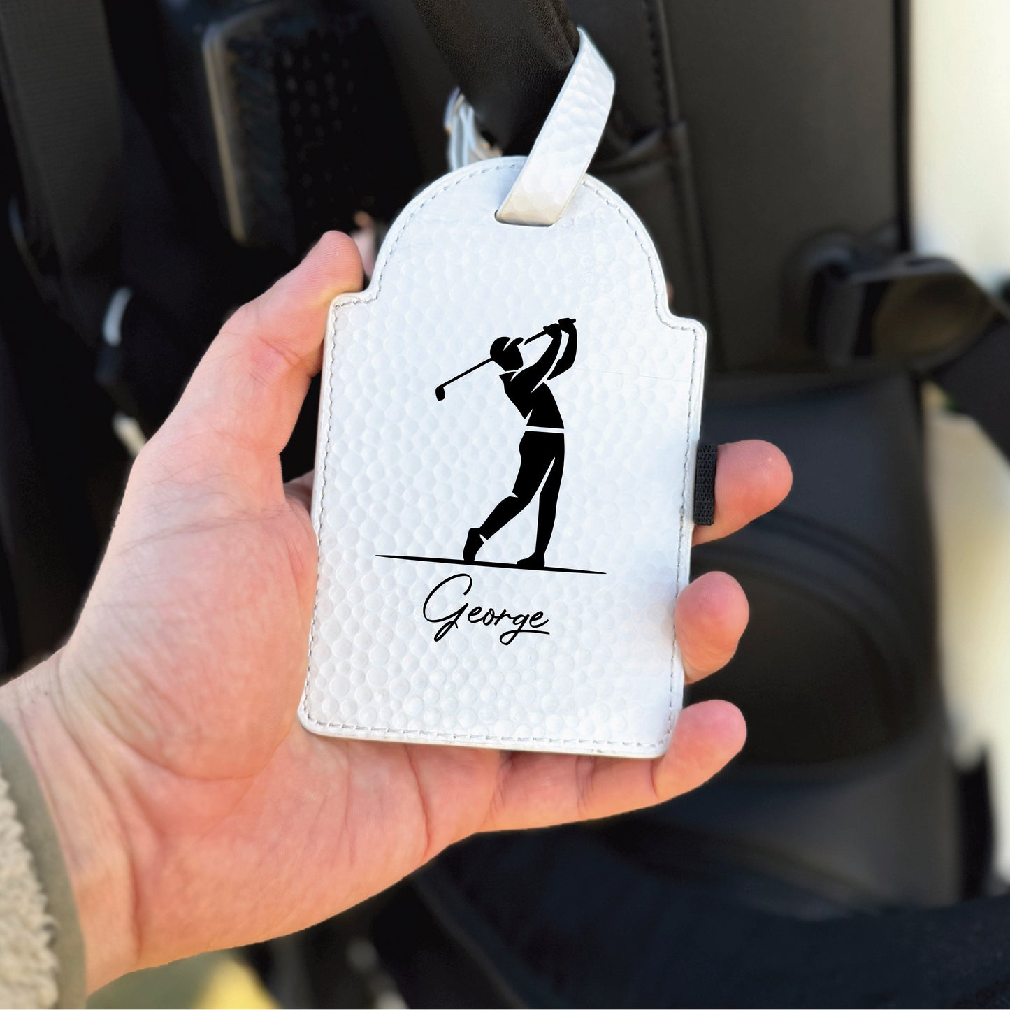 White leather luggage tag with golf swing silhouette and sample name "George" engraved below
