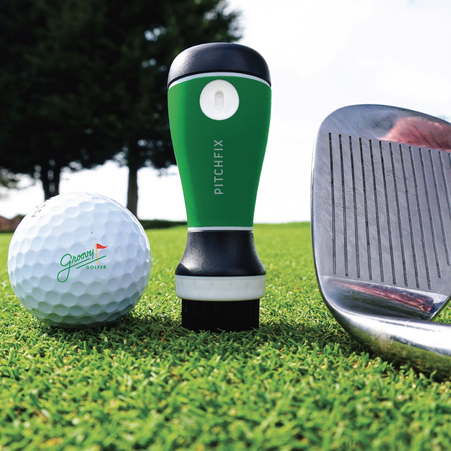 Green and black golf gift set on grass featuring personalized golf ball with sample "Groovy Golfer" text, PitchFix divot tool, and golf club head
