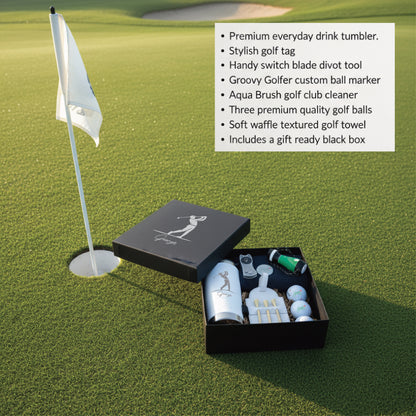 Golf gift set displayed on putting green with tumbler, golf balls, tees, divot tool, ball marker, and towel in black gift box