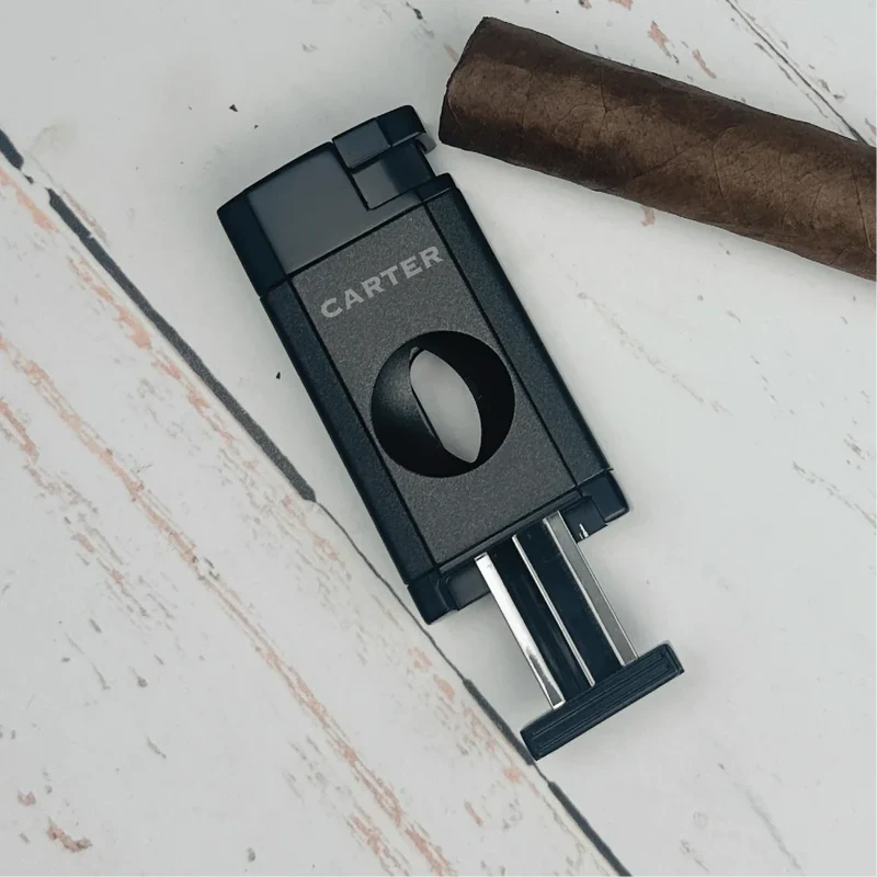 Black dual-flame cigar cutter with "Carter" engraving and stainless steel blades, displayed next to a brown cigar on whitewashed wood.