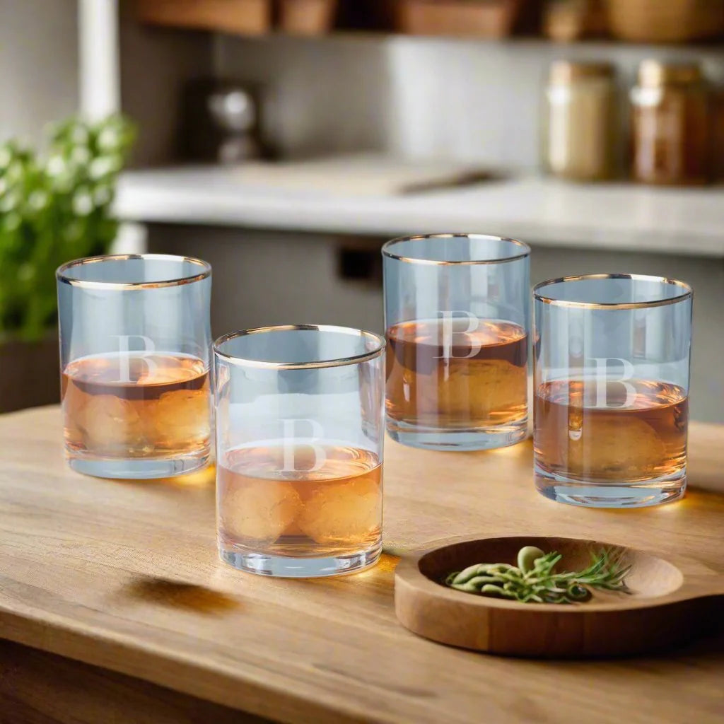 Four glass tumblers with gold rims on a wooden surface in a kitchen setting.