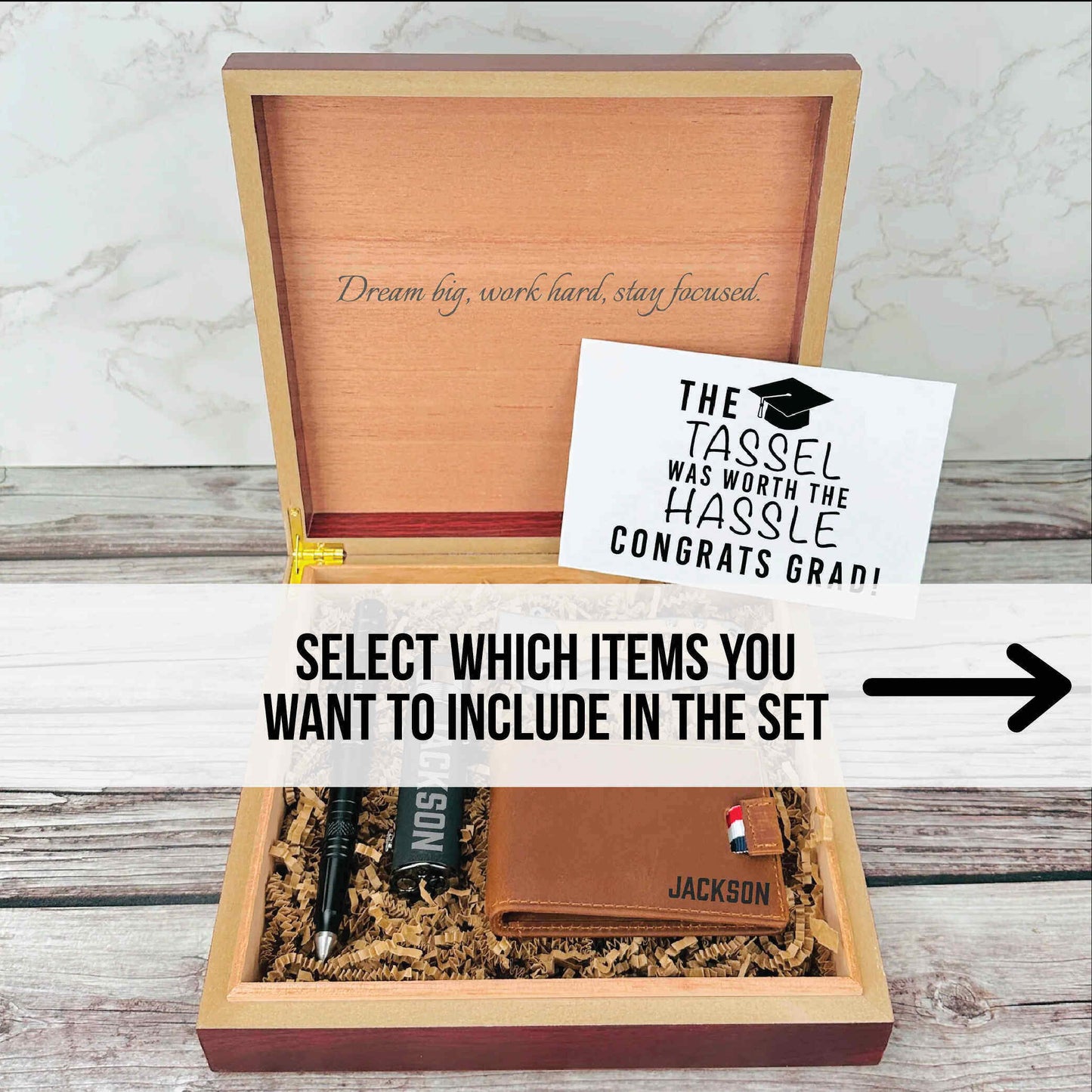 Wooden box with engraved "Dream big, work hard, stay focused" on lid, containing sample personalized leather wallet with name "Jackson" and other gift items.