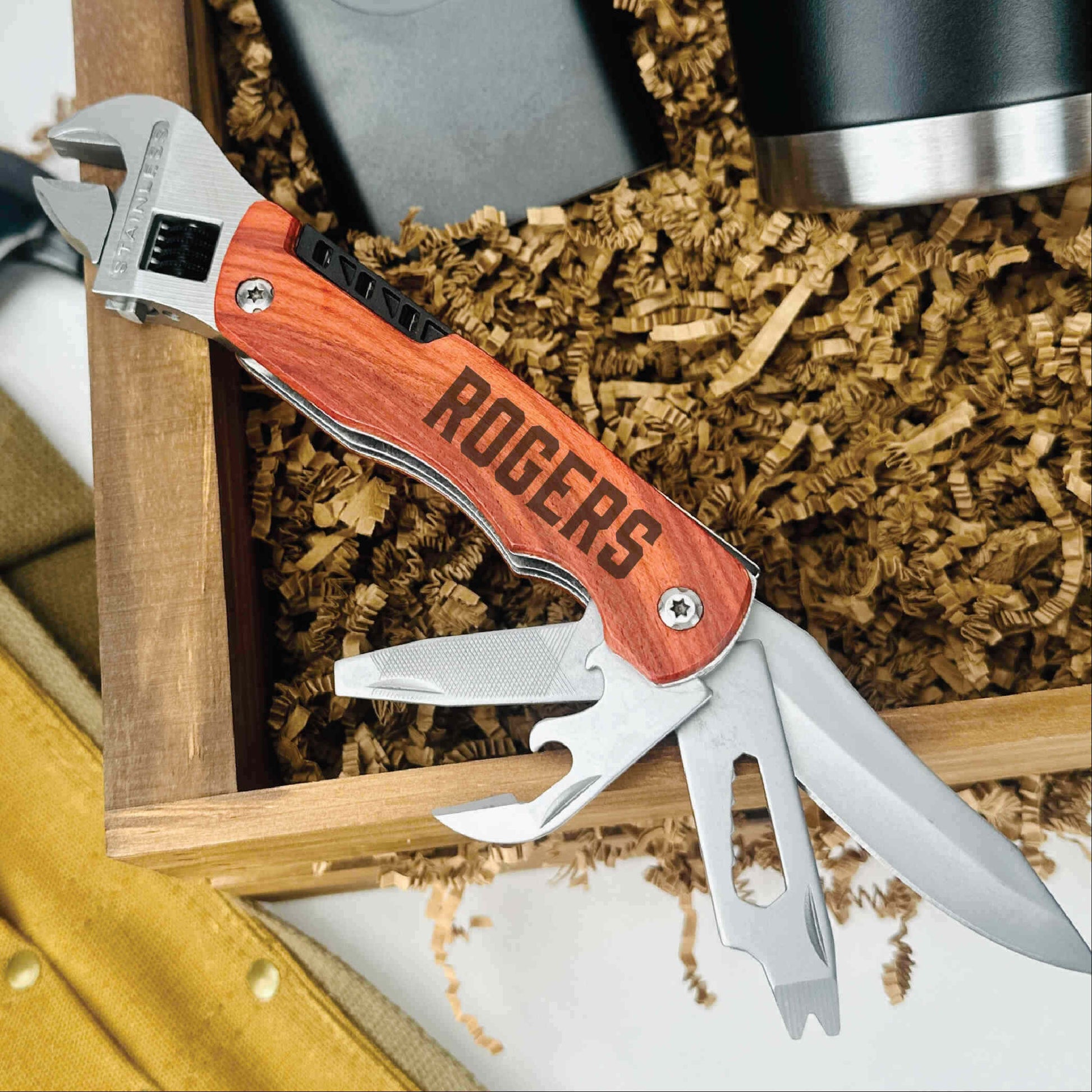 Multi-tool with engraved wood handle reading "ROBERTS" displayed in gift box with packing material and flask.