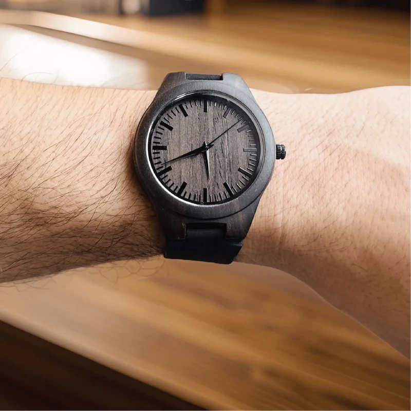 Black wooden watch with minimalist dial and index markers worn on wrist against natural wood background